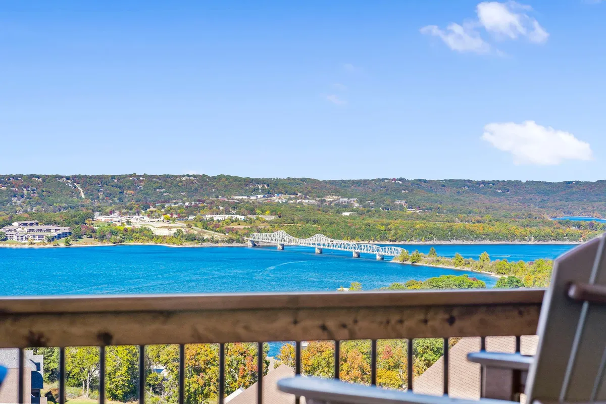A serene, wide-angle view of Table Rock Lake with a prominent bridge crossing over sparkling water and gently rolling, tree-lined hills in the distance. The sky is expansive, creating a tranquil lakeside atmosphere perfect for water activities.