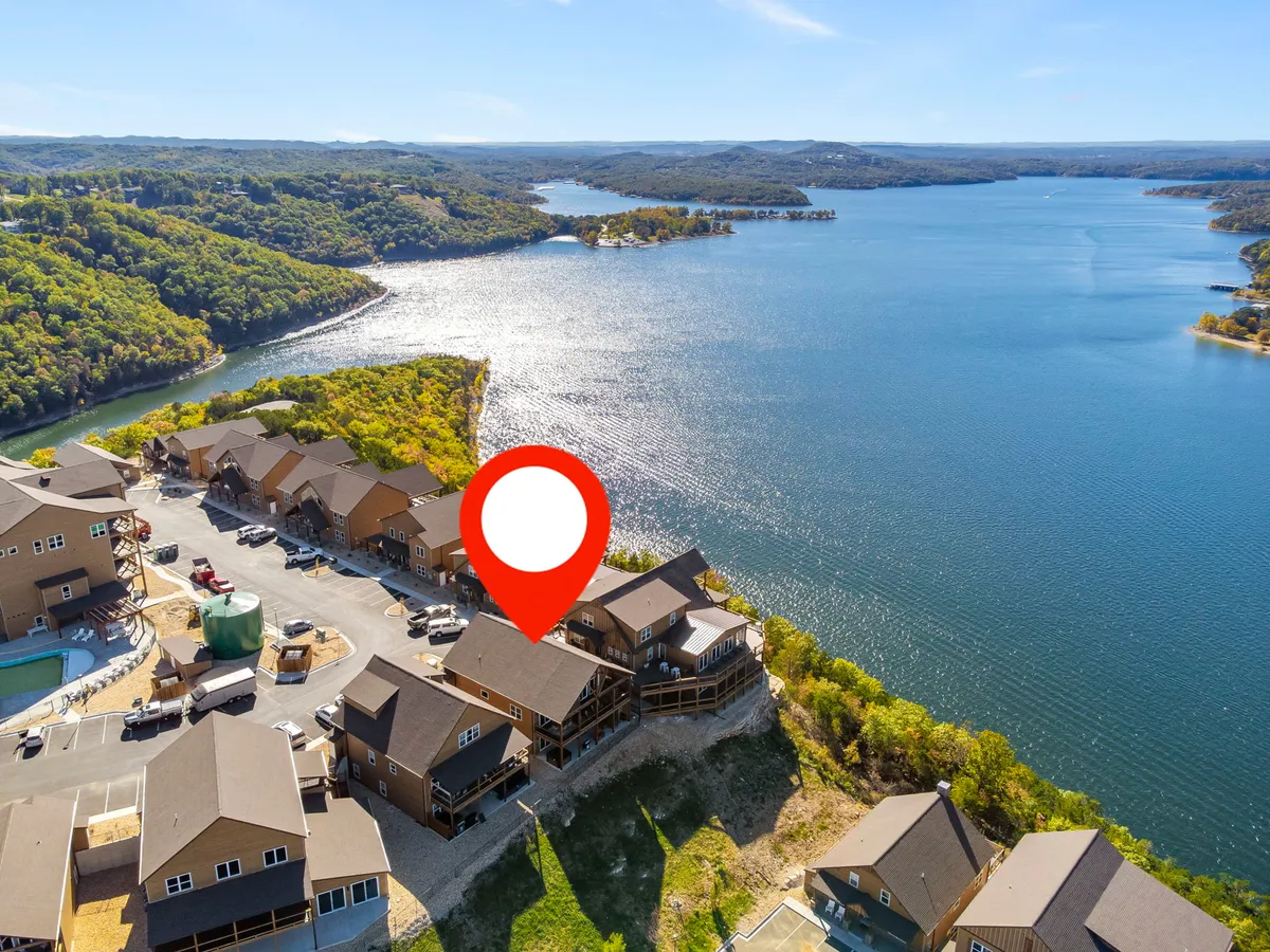 A peaceful lakeside setting with calm water, houses along the shore, and tree-covered hills in the distance. The view evokes the natural beauty and outdoor recreational opportunities of the Ozarks region, inviting exploration and relaxation.