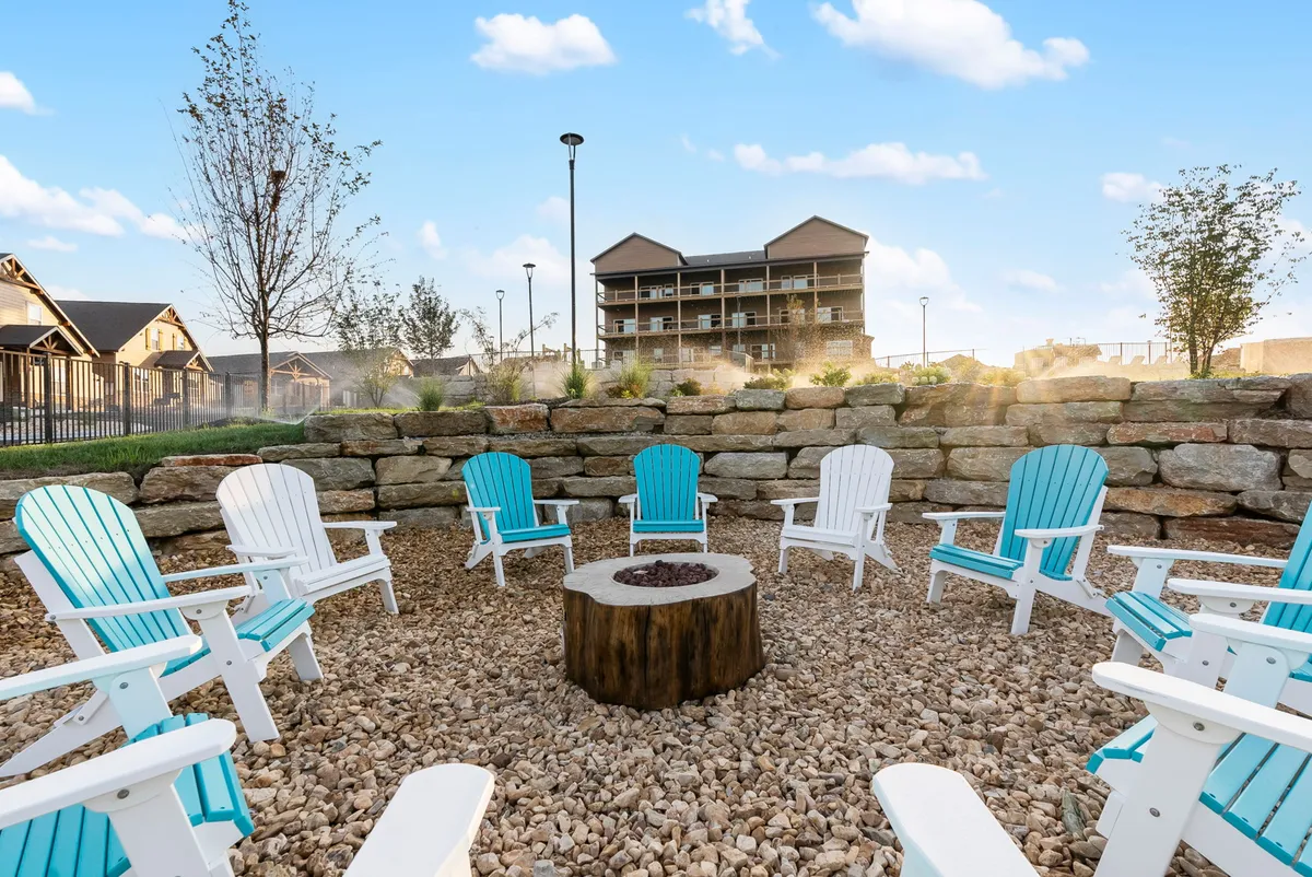 An inviting exterior shot of a communal fire pit ringed with Adirondack chairs and set against a stone wall, evoking a cozy, communal atmosphere perfect for evening gatherings or storytelling under the stars.