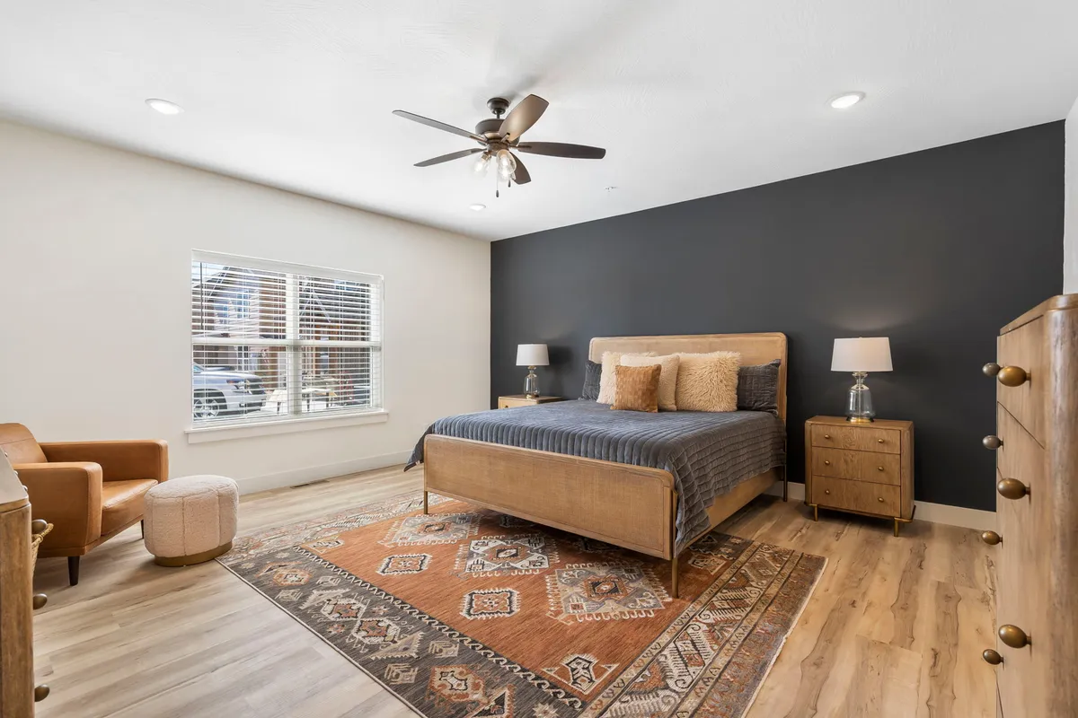 A serene queen or king bedroom with a comfortable bed, decorative pillows, a soft area rug, a window letting in sunlight, and an inviting armchair for reading or relaxing.