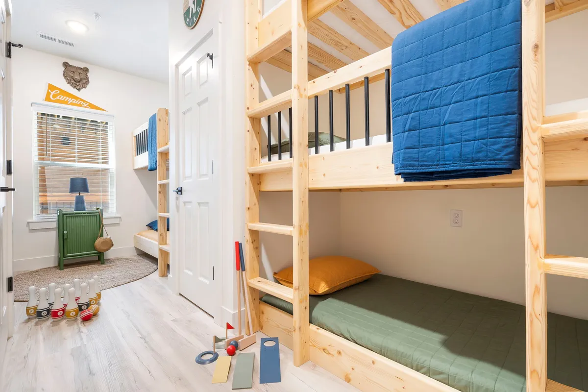 A cheerful bunk room featuring colorful bunk beds, a green side table, playful bowling pins, and soft textiles. The space feels playful, relaxed, and perfect for kids to enjoy sleepovers and playful activities.