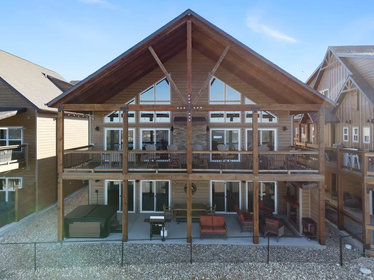 A spacious wooden deck furnished with multiple seating areas and bordered by a sturdy railing. Large sliding glass doors connect the indoor space to the deck, and the vantage point suggests views overlooking the lake or surrounding nature.