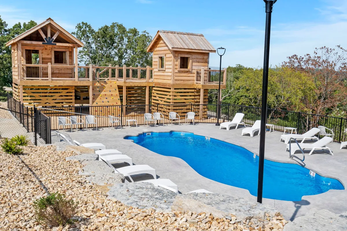 This exterior image captures a lively scene with wooden playhouses, a sparkling swimming pool, and lounge chairs, evoking the joyful and playful ambiance of summer gatherings. Kids are seen playing in the playhouses, while adults and families can be imagined enjoying the refreshing pool and relaxing poolside.